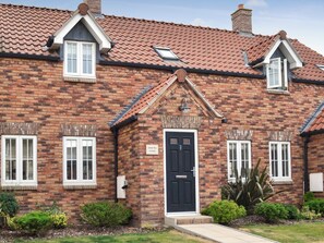 A brick cottage with a black front door, white-framed windows, a small porch, and a chimney.