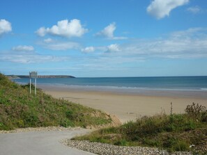 A coastal road leading to a beach with a signpost and rocky terrain.
