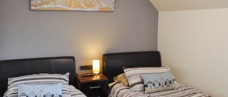 A bedroom with two beds, striped bedding, a beach-themed pillow, a bedside lamp, and a painting of a beach scene.