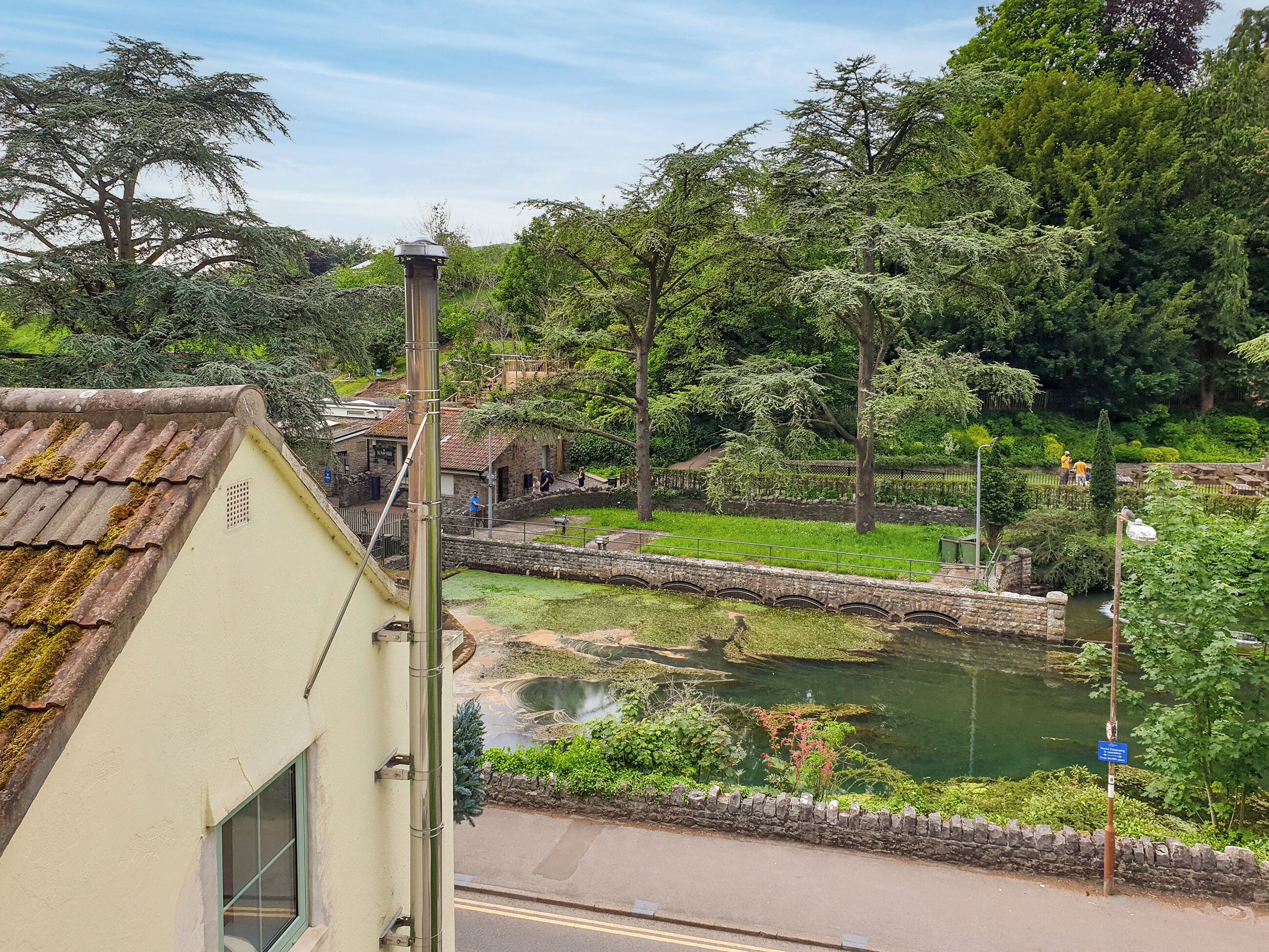 A riverside park with stone walls, a small bridge, and lush greenery.