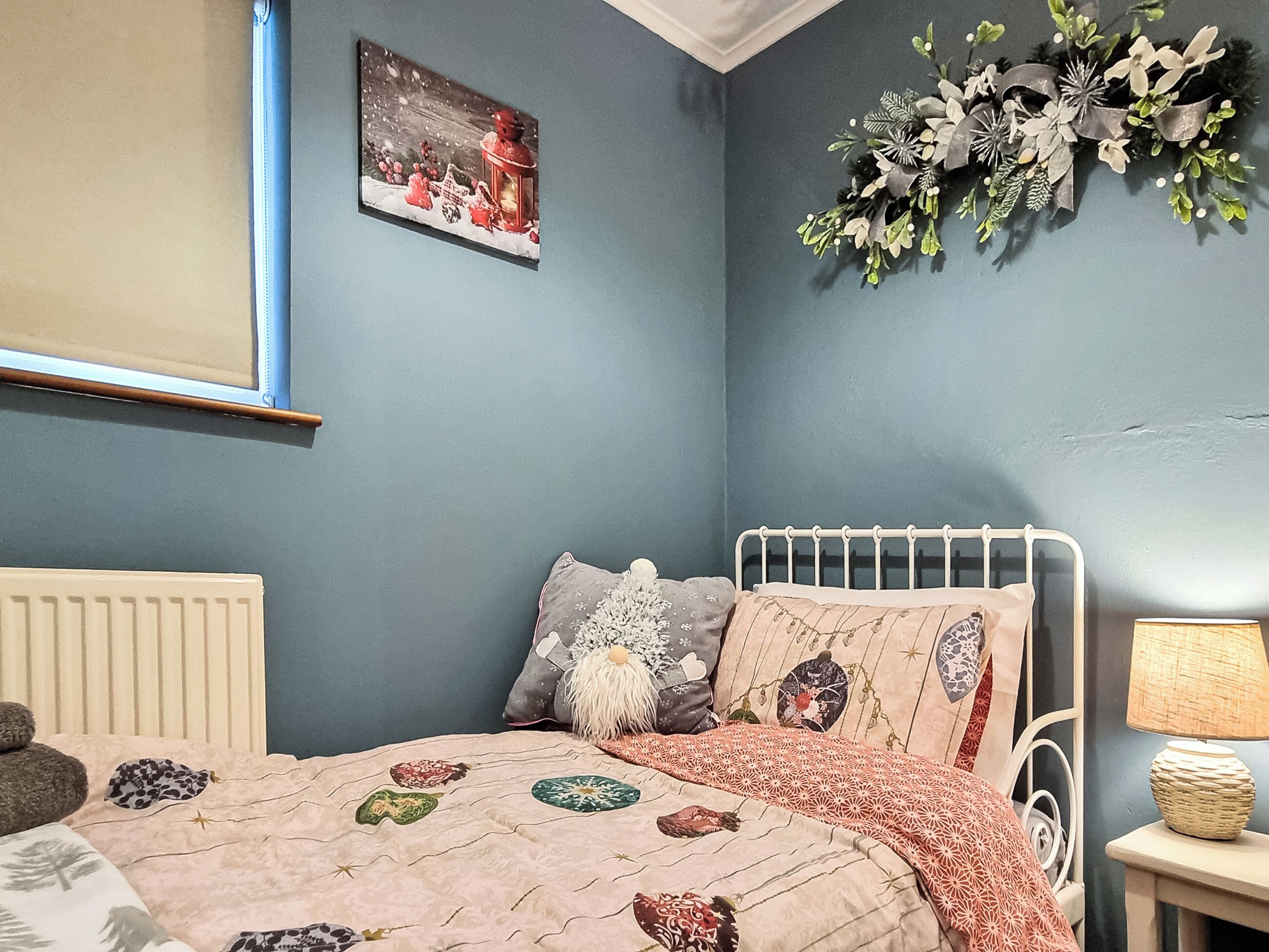 Une chambre à coucher avec un lit, des oreillers, une table de chevet, une lampe, un radiateur et un élément de décoration murale.