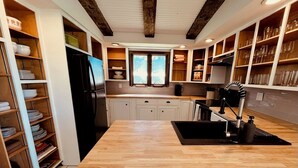 Une cuisine avec des armoires en bois, un réfrigérateur noir, un plan de travail en bois et une fenêtre.