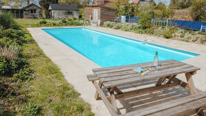 En rektangulär swimmingpool med ett trädäck och ett picknickbord med en flaska och ett glas.