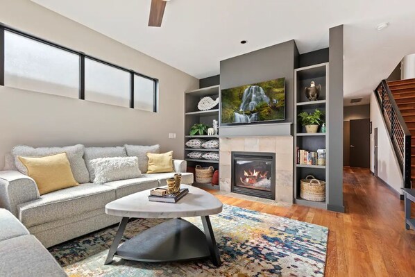 A modern living room with a grey sofa, a coffee table, a fireplace, and a bookshelf. - Lux Home w/ Hot Tub+Fire Pit steps from Hyde Park (Boise)
