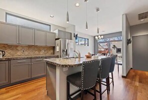 A modern kitchen with grey cabinets, a granite countertop island, and bar stools. - Lux Home w/ Hot Tub+Fire Pit steps from Hyde Park (Boise)