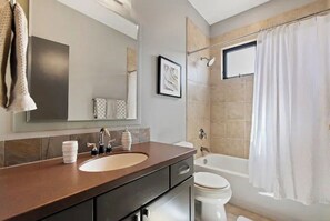 A modern bathroom with a beige sink, a large mirror, a framed picture on the wall, a bathtub, and a shower curtain. - Lux Home w/ Hot Tub+Fire Pit steps from Hyde Park (Boise)
