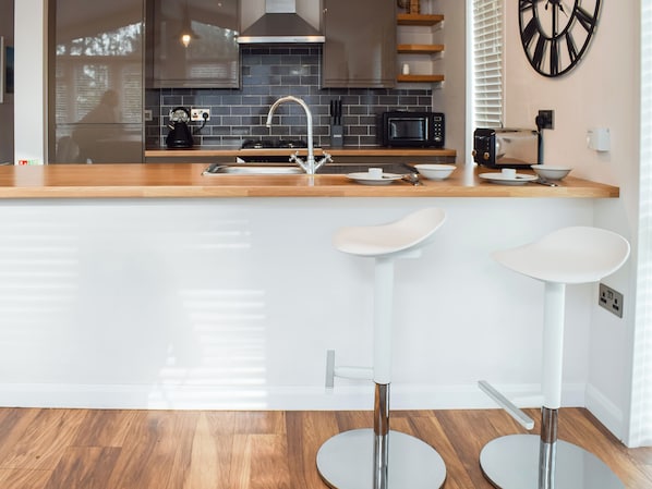 A modern kitchen with a wooden countertop, stainless steel sink, and two white bar stools.