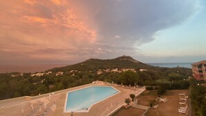 A swimming pool with lounge chairs and umbrellas, surrounded by greenery and a hill with buildings in the background. - Ideally located 4-person apartment with exceptional view (Saint-Raphaël)