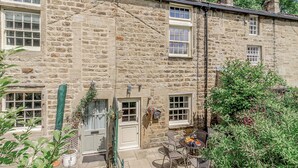 A stone building with multiple windows, a door, and a small outdoor seating area with chairs and a table. - 3 bedroom accommodation in Bewerley, near Pateley Bridge (Bewerley, near Pateley Bridge)