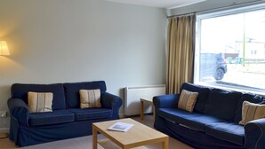 A living room with two dark blue sofas, a wooden coffee table, and a window with curtains. - 3 bedroom accommodation in Newton by the Sea (Newton by the Sea)