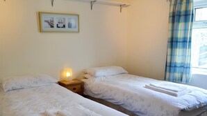 A hotel room with two single beds, a nightstand with a lamp, a framed picture on the wall, and a window with curtains. - 3 bedroom accommodation in Newton by the Sea (Newton by the Sea)