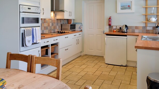 A kitchen with white cabinets, a microwave, an oven, a sink, and a wooden dining table with chairs. - 3 bedroom accommodation in Newton by the Sea (Newton by the Sea)