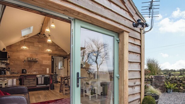 Una cabaña acogedora con una cocina moderna, un comedor y una sala de estar con un sofá de cuero y un tapete rojo.