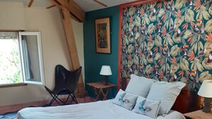 Un dormitorio con una cama de madera, una silla, una mesita, una lámpara, un cuadro y una ventana.