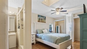 Een slaapkamer met een bed, een dressoir, een plafondventilator en een schilderij aan de muur.