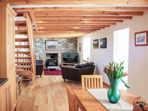 A wooden staircase leading to a living area with a stone fireplace, a television, and a dining table with a vase of flowers.