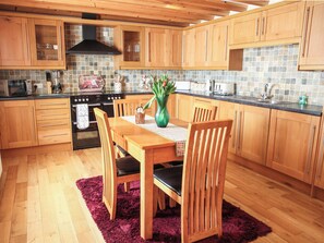 Une cuisine avec des meubles de rangement en bois, une cuisinière et une table à manger avec des chaises.
