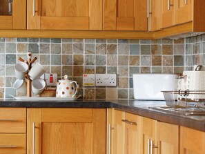 A kitchen with wooden cabinets, a tiled backsplash, a kettle, a toaster, and a basket of cups.