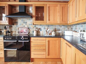 A kitchen with wooden cabinets, a stove, and a tiled backsplash. - 2 bedroom accommodation in Strathkanaird, Ullapool (Strathkanaird, Ullapool)