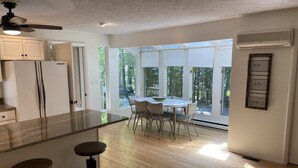 Eine moderne Küche mit einer zentralen Kochinsel, Barhocker, einem Essbereich mit Tisch und Stühlen sowie großen Fenstern mit Blick ins Freie.