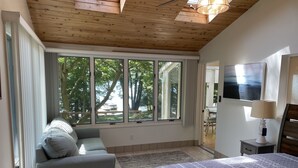 Ein Schlafzimmer mit einem großen Bett, einer Couch, einem Fernseher und einem Fenster mit Blick auf Bäume.