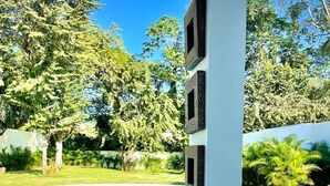 Un canapé en osier avec des coussins blancs, placé dans un espace extérieur abrité, avec vue sur une piscine.