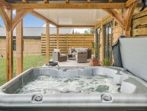 A hot tub area with a wooden deck, wicker furniture, and a view of a house in the background. - Bramley Lodge - UK38384 (Lyonshall, near Kington)