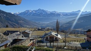 A mountain village with traditional houses, a clear sky, and snow-capped peaks in the background.