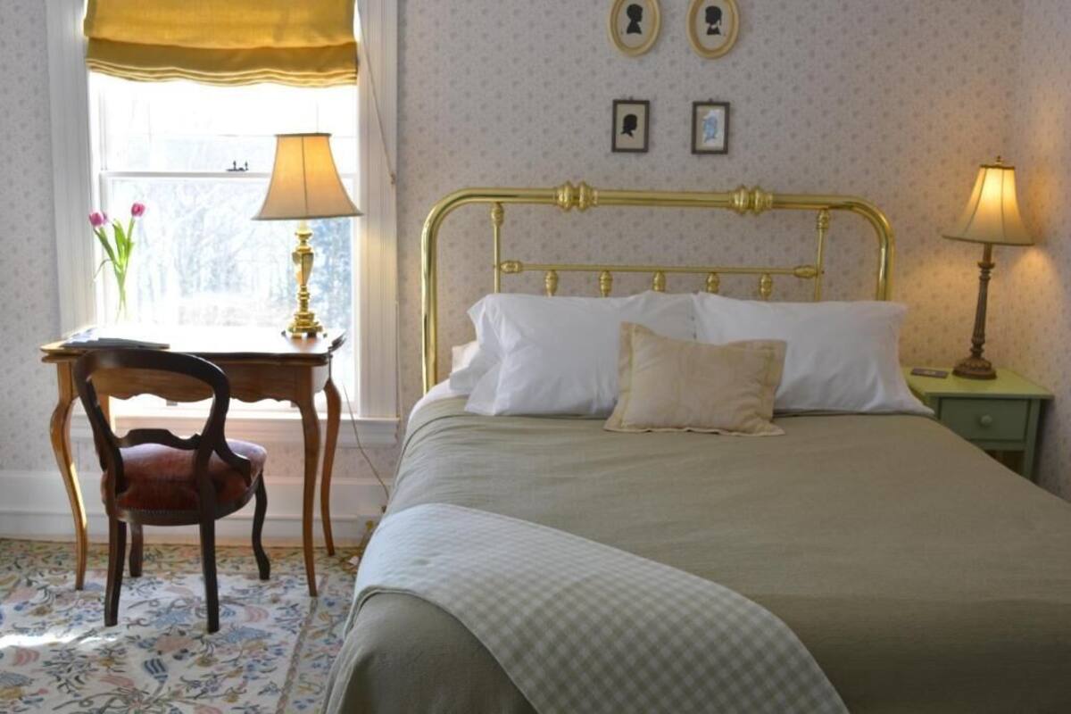 Un dormitorio ordenado con una cama clásica, un escritorio de madera y una silla.
