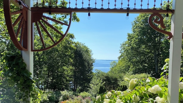 Un espacio de estar cubierto al aire libre con una mesa dispuesta para dos, con vistas a un jardín y al mar.
