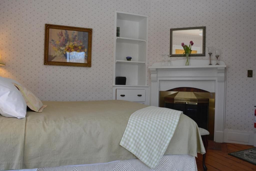 A bedroom with a bed, a white dresser, a mirror, a fireplace, and a wall-mounted shelf.