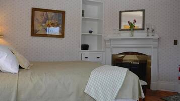 A bedroom with a bed, a white dresser, a mirror, a fireplace, and a wall-mounted shelf.