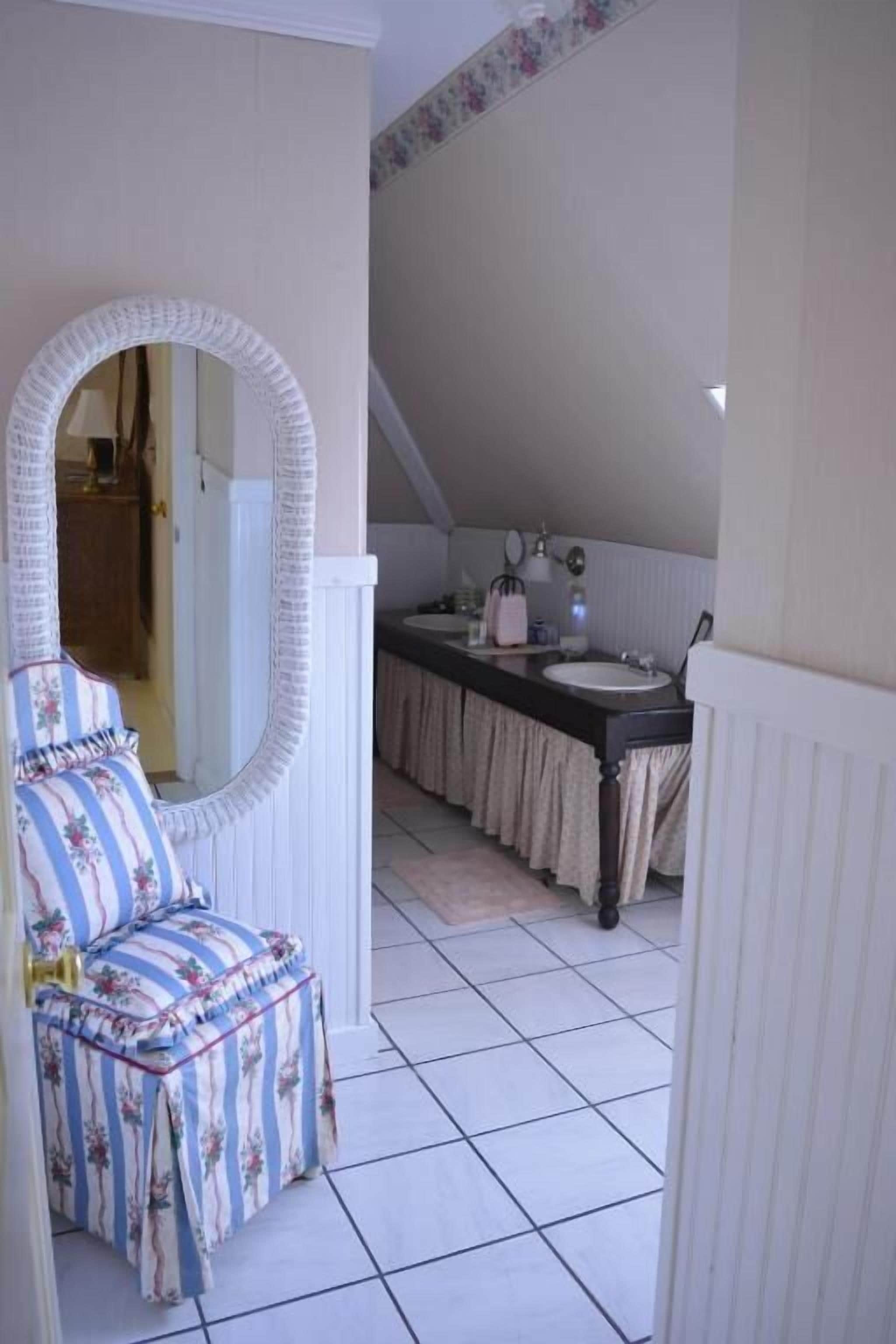 Ein Schlafzimmer mit einem großen Spiegel, einem Bett mit floralem Bettbezug, einem Waschtisch mit Waschbecken und einem Fenster mit Blick ins Freie.