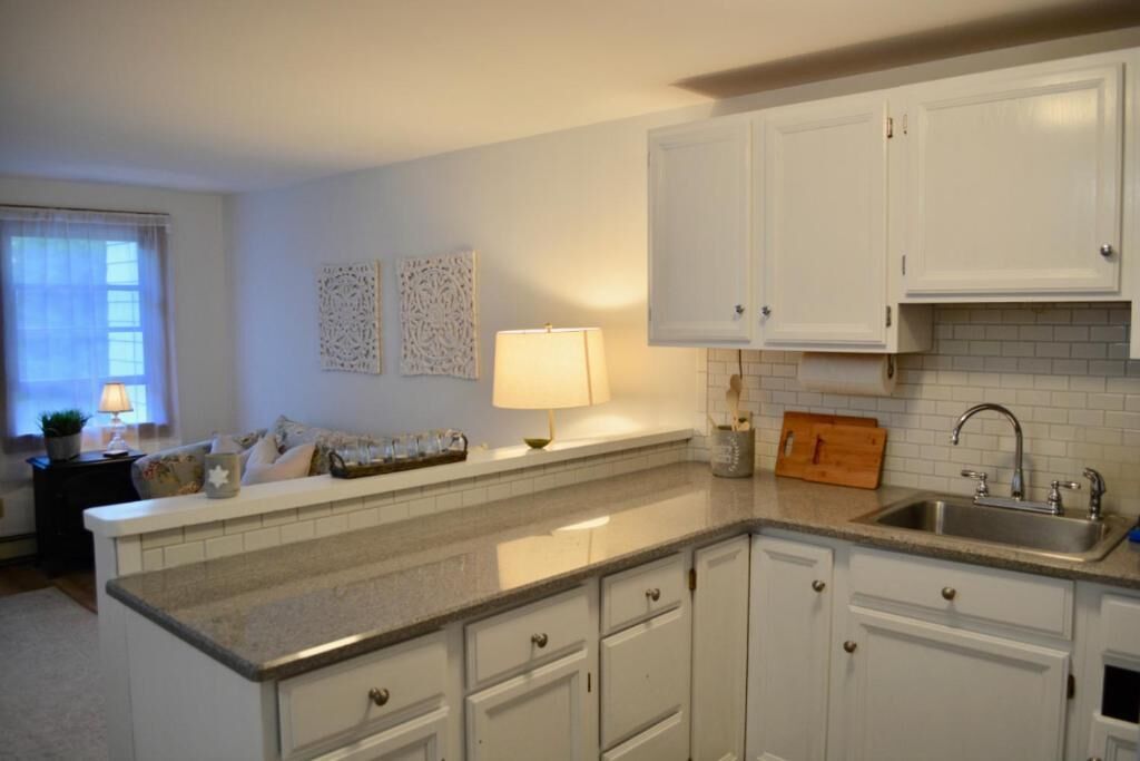 A kitchen with white cabinets, a countertop, a sink, and a window with curtains.