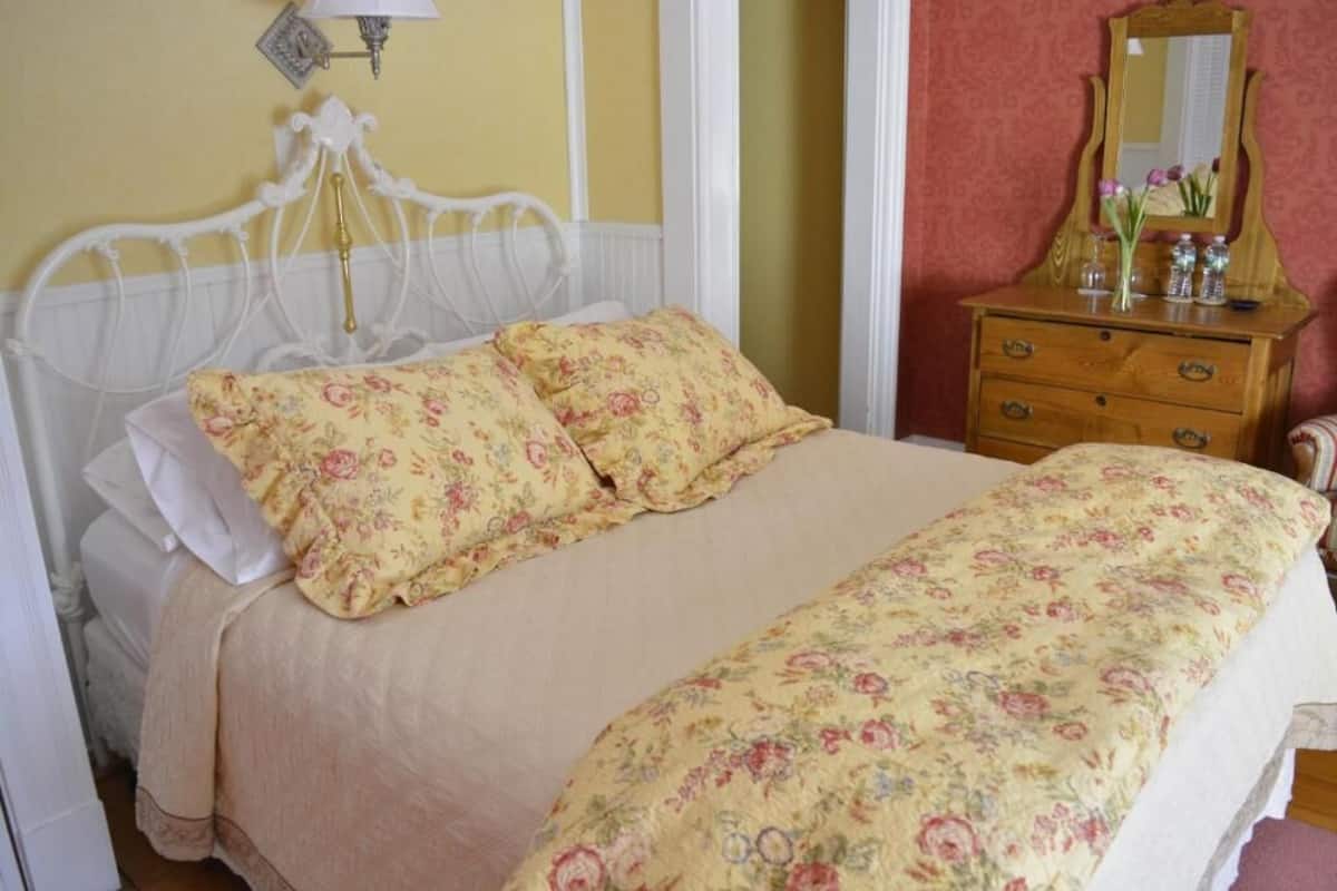 Una cama con ropa de cama floral, un tocador de madera con espejo y una lámpara de pared.