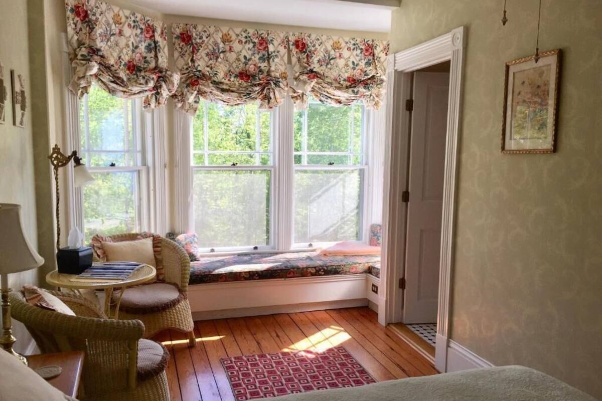 Una habitación acogedora con un asiento junto a la ventana, muebles de mimbre y una puerta que da al exterior.