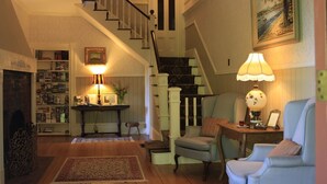 Un salón acogedor con una escalera, una estantería, una mesa con una lámpara y un sillón.