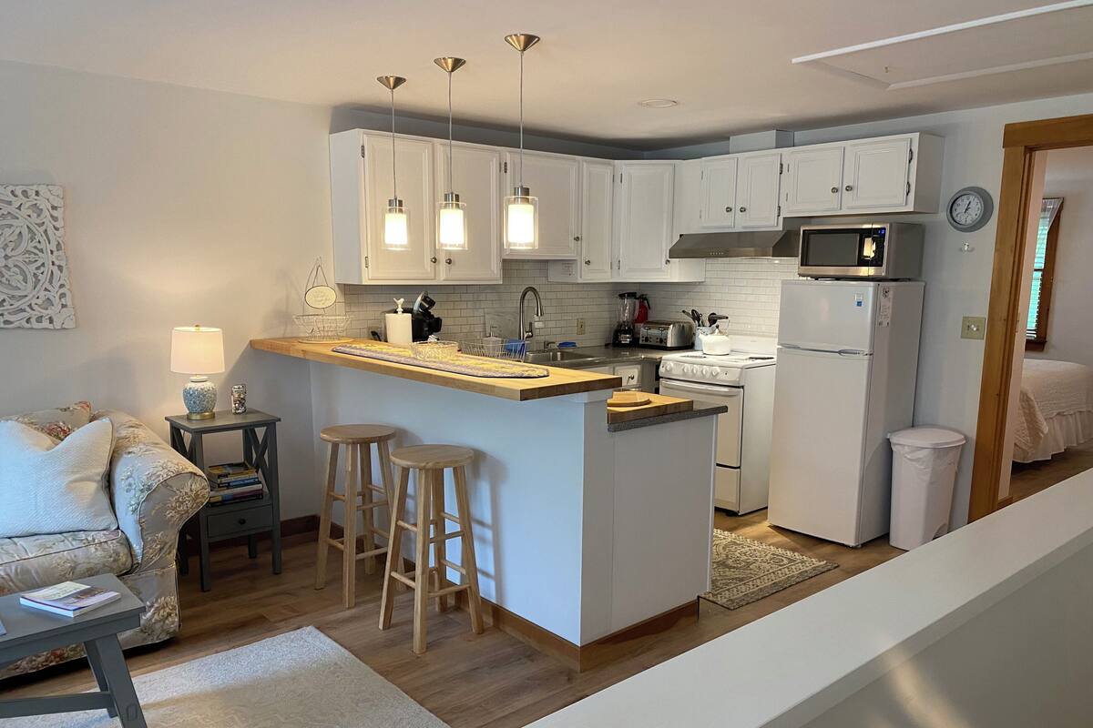 Una cocina moderna con armarios blancos, una isla central con taburetes, microondas y refrigerador.
