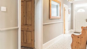 A hallway with a wooden door, a mirror, and a patterned floor. - 3 bedroom accommodation in Beccles (Beccles)