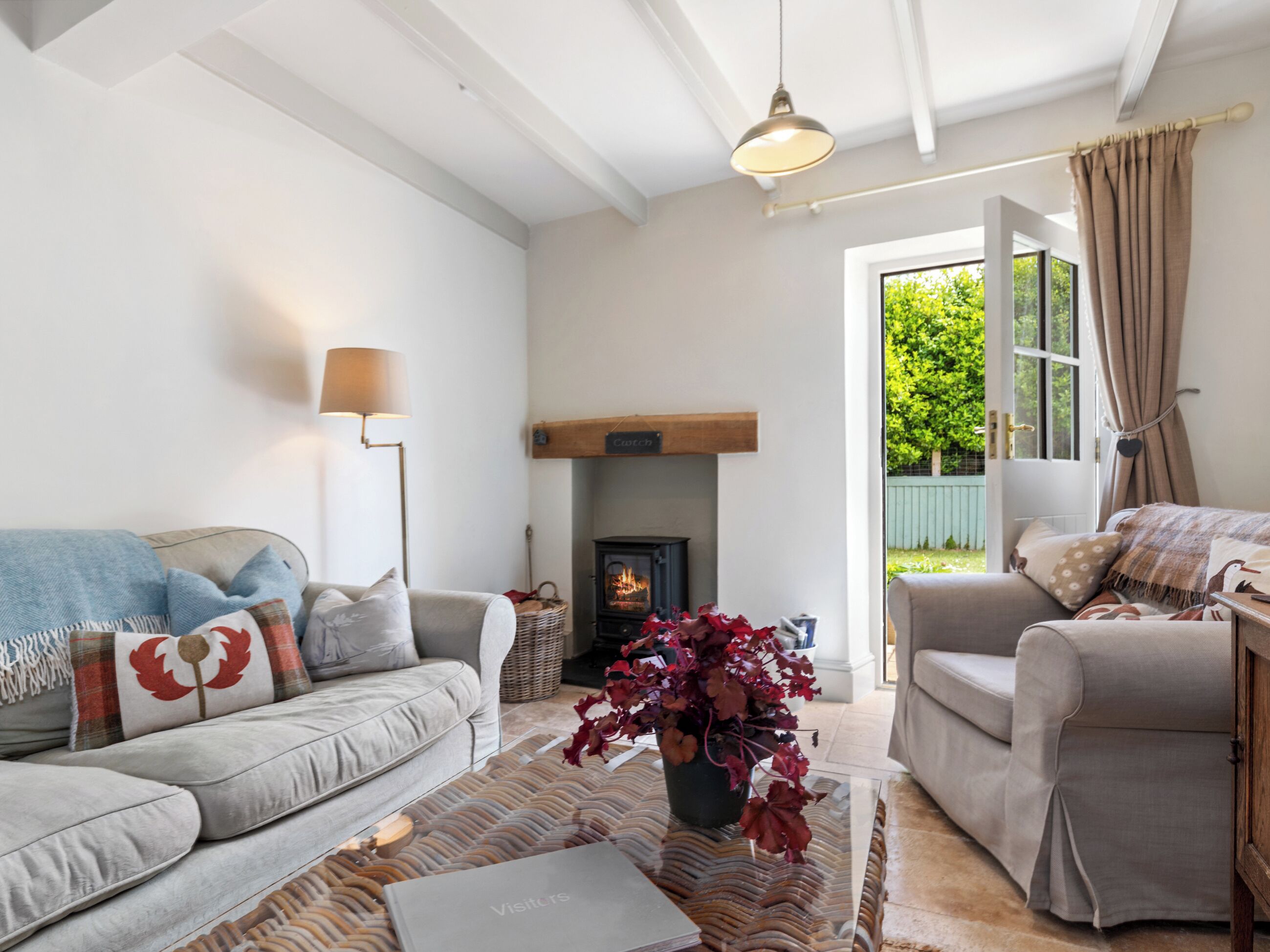 A cozy living room with a sofa, a coffee table, a fireplace, and a view of greenery outside.