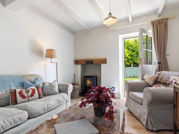 A cozy living room with a sofa, a coffee table, a fireplace, and a view of greenery outside.
