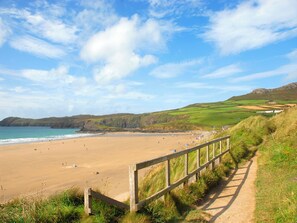 A coastal beach with a wooden fence, grassy hills, and a clear sky.