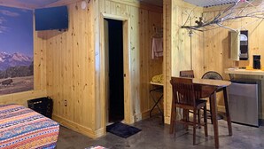 A cozy cabin-style room with a bed, a small dining table, and a kitchenette.