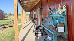 A rustic outdoor seating area with wooden tables and chairs, a blue-painted wooden shelf with decorative items, and a sign reading "FRESH EGGS".
