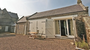 A stone building with a gravel driveway, a wooden table and chairs, and a sliding glass door.