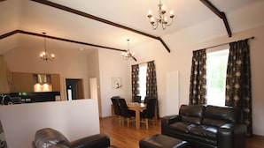 A spacious living area with leather sofas, a dining table, and a kitchen in the background.
