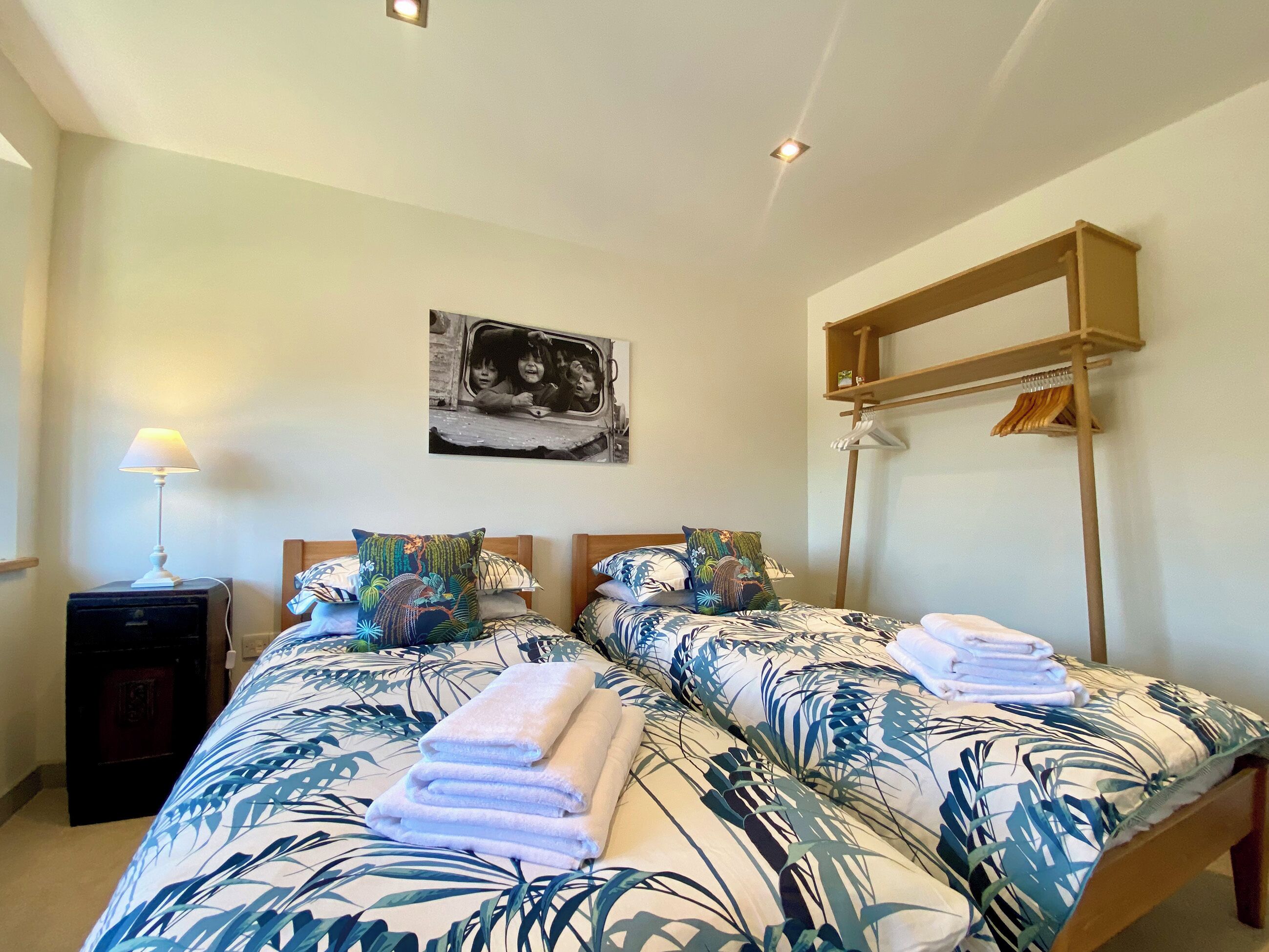Un dormitorio con dos camas, una mesita de noche, una lámpara, un estante en la pared y un cuadro.