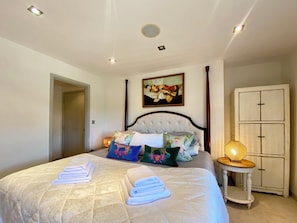 Un dormitorio con cama, almohadas, una mesita de noche con lámpara, un armario y un cuadro en la pared.