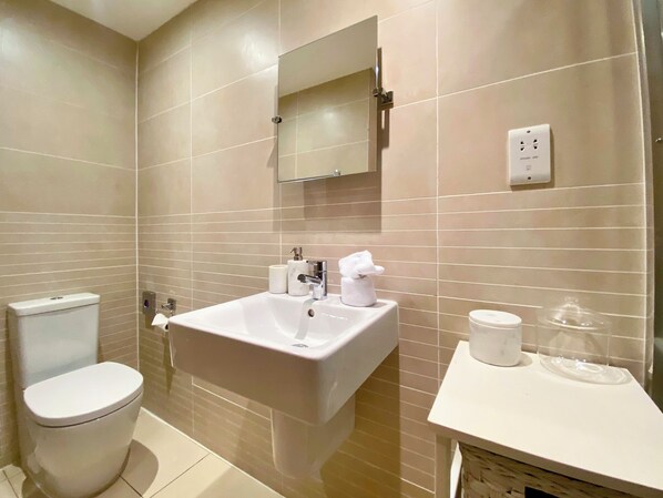 A bathroom with a toilet, sink, mirror, and a small countertop with a tissue dispenser.