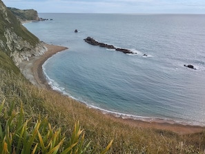 Eine Küstenlandschaft mit einer gewundenen Strandlinie, Felsenformationen und grasbewachsenem Gelände.